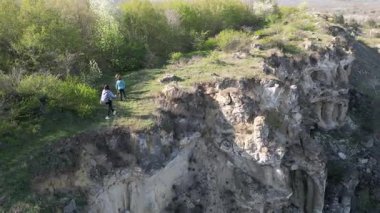 Güneşli bir günde bir anne ve iki çocuk manzaralı bir uçurumun kenarında yürüyüş yaparlar. Manzara engebeli ve vahşi, dramatik kaya oluşumları ve yeşil bahar bitkileriyle.