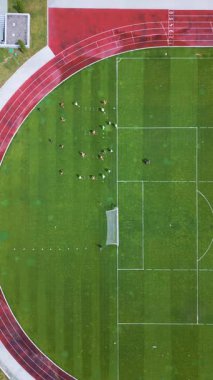 Yeşil bir futbol sahasında oyuncuların antrenman yaptığı bir futbol antrenmanının hava görüntüsü. Koşu pisti ve kale direği görünüyor. Spor pratiği ve takım çalışması konsepti.