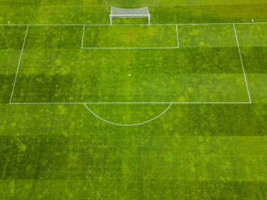 Beyaz işaretli yeşil bir futbol sahası ve tek bir kale direği. Çimenler biçme şekillerini gösteriyor. Yüzeyde çizgili bir doku oluşturuyor. Boş ve iyi korunmuş ses tonu.