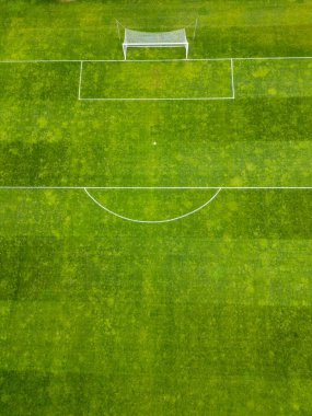 Beyaz işaretli yeşil bir futbol sahası ve tek bir kale direği. Çimenler biçme şekillerini gösteriyor. Yüzeyde çizgili bir doku oluşturuyor. Boş ve iyi korunmuş ses tonu.