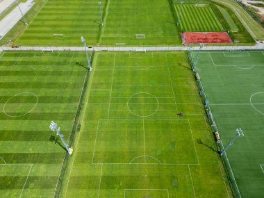 Bir spor kompleksindeki çoklu futbol sahalarının havadan görüntüsü. Bazılarında eğitim çizgileri, bazılarında standart işaretler var. Yeşil çimenler, yapay çim, tenis kortu ve görünür projektörler..