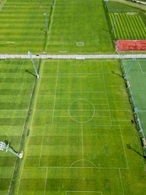 Bir spor kompleksindeki çoklu futbol sahalarının havadan görüntüsü. Bazılarında eğitim çizgileri, bazılarında standart işaretler var. Yeşil çimenler, yapay çim, tenis kortu ve görünür projektörler..