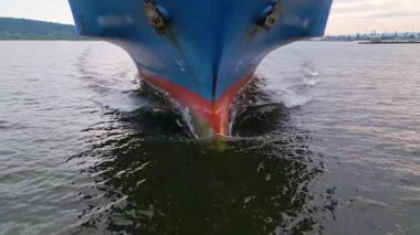 Büyük bir kargo gemisinin pruvasının, suyu keserek dalgalar oluşturduğu yakın çekim görüntüsü. Deniz taşımacılığı ve taşımacılık endüstrisi hareket halinde.