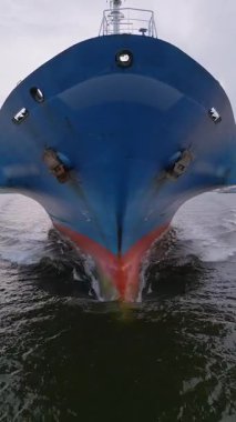 Büyük bir kargo gemisinin pruvasının, suyu keserek dalgalar oluşturduğu yakın çekim görüntüsü. Deniz taşımacılığı ve taşımacılık endüstrisi hareket halinde.