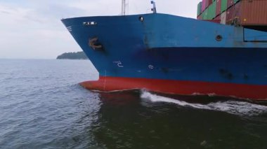 Denizde ilerleyen büyük mavi bir kargo gemisinin yan görüntüsü, su hattının altında pruva, çapa ve kırmızı gövdeyi gösteriyor. Deniz taşımacılığı ve uluslararası nakliye kavramı.