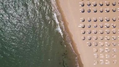Saman şemsiyeleri ve güneş yatakları sıra sıra dizilmiş, dalgalar yavaşça kıyıya vuruyor. Yaz tatili kavramı.