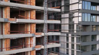 İnşaat halindeki iki modern konut binasının yakın görüntüsü. Bir cephe cam pencerelerle tamamlanmış, diğeri ise görülebilir beton ve tuğlalarla tamamlanmamış. Kentsel gelişim sahnesi.