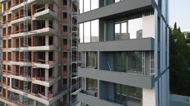 İnşaat halindeki iki modern konut binasının yakın görüntüsü. Bir cephe cam pencerelerle tamamlanmış, diğeri ise görülebilir beton ve tuğlalarla tamamlanmamış. Kentsel gelişim sahnesi.