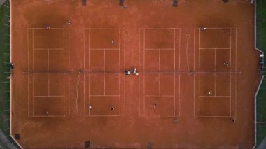 Oyuncuların pratik yaptığı kırmızı kil tenis kortlarının yukarıdan aşağı görüntüsü. Güneşli bir günde çizgiler, ağlar ve görünür eğitim aktiviteleriyle simetrik spor düzeni.