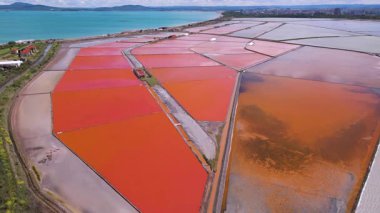 Bulgaristan 'ın Burgaz kenti yakınlarındaki renkli tuz tavalarının hava manzarası. Canlı kırmızı ve turuncu buharlaşma, beyaz tuz yığınları ve turkuaz deniz ile tezat oluşturur. Sanayi ve doğal güzelliğin birleşimi.
