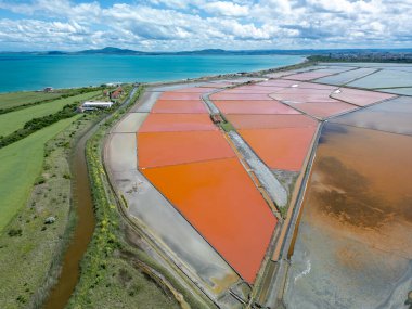 Bulgaristan 'ın Burgaz kenti yakınlarındaki renkli tuz tavalarının hava manzarası. Canlı kırmızı ve turuncu buharlaşma, beyaz tuz yığınları ve turkuaz deniz ile tezat oluşturur. Sanayi ve doğal güzelliğin birleşimi.