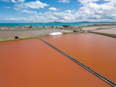 Bulgaristan 'ın Burgaz kenti yakınlarındaki renkli tuz tavalarının hava manzarası. Canlı kırmızı ve turuncu buharlaşma, beyaz tuz yığınları ve turkuaz deniz ile tezat oluşturur. Sanayi ve doğal güzelliğin birleşimi.