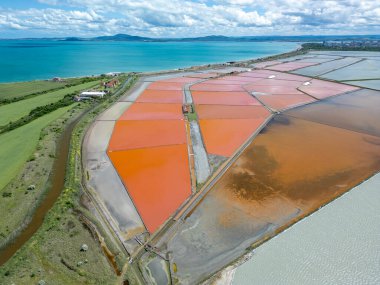 Bulgaristan 'ın Burgaz kenti yakınlarındaki renkli tuz tavalarının hava manzarası. Canlı kırmızı ve turuncu buharlaşma, beyaz tuz yığınları ve turkuaz deniz ile tezat oluşturur. Sanayi ve doğal güzelliğin birleşimi.