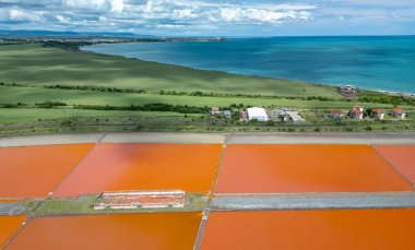 Bulgaristan 'ın Burgaz kenti yakınlarındaki renkli tuz tavalarının hava manzarası. Canlı kırmızı ve turuncu buharlaşma, beyaz tuz yığınları ve turkuaz deniz ile tezat oluşturur. Sanayi ve doğal güzelliğin birleşimi.