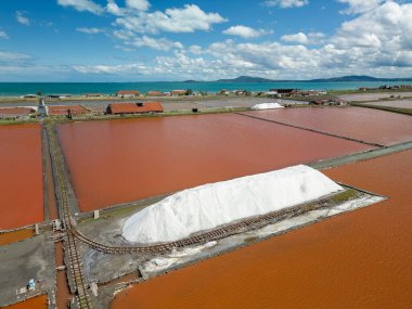 Bulgaristan 'ın Burgaz kenti yakınlarındaki renkli tuz tavalarının hava manzarası. Canlı kırmızı ve turuncu buharlaşma, beyaz tuz yığınları ve turkuaz deniz ile tezat oluşturur. Sanayi ve doğal güzelliğin birleşimi.