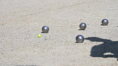 Arka arkaya iki Petanque, metal topların parlak sarı krikonun yakınına düştüğü, geleneksel Fransız oyununda strateji ve hassasiyet sergilediği çakıl taşı kortuna fırlatıyor..