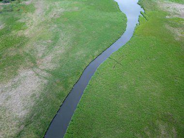 Dar bir nehrin, yemyeşil sulak bir arazide kıvrılışının havadan görüntüsü. Durgun su, canlı bitki örtüsüyle çelişiyor, yukarıdan sakin ve doğal bir manzara yaratıyor..