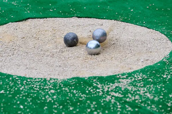 Petanque hassas atış müsabakası. Metal toplar kumda hedefe çarpıyor. Çarpışma anında toz bulutu uçuyor. Doğruluk ve dinamik oyuna odaklan.