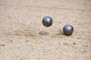 Uçan petanque topu yere düştü, kumlu bir arazide, dinamik bir atışta havaya çakıl gönderdi..