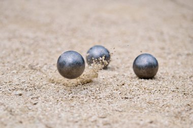 Uçan petanque topu yere düştü, kumlu bir arazide, dinamik bir atışta havaya çakıl gönderdi..