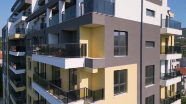 Temiz mimarisi, geniş pencereleri ve balkonları olan, temiz mavi gökyüzü altında kentsel bir ortamda kurulmuş, modern bir konut binasının yörüngesindeki hava aracı görüntüsü..