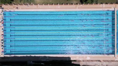 Açık havada olimpiyat boyutunda bir yüzme havuzunun havadan görünüşü ve şeritlerde birden fazla yüzücü eğitimi. Gündüz İHA 'dan yakalanmış. Spor, spor, spor ve eğlence teması için ideal..