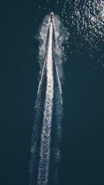 Koyu mavi suda hızla ilerleyen bir jet ski 'nin havadan görünüşü, dinamik beyaz bir iz bırakıyor. Yukarıdan insansız hava aracı tarafından ele geçirildi. Denizde hareketlilik, güç ve yaz eğlencesi sergileniyor..
