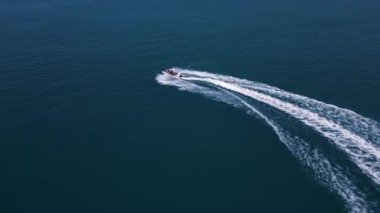 Koyu mavi suda hızla ilerleyen bir jet ski 'nin havadan görünüşü, dinamik beyaz bir iz bırakıyor. Yukarıdan insansız hava aracı tarafından ele geçirildi. Denizde hareketlilik, güç ve yaz eğlencesi sergileniyor..