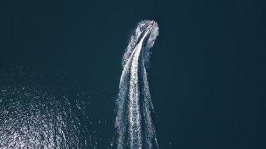 Koyu mavi suda hızla ilerleyen bir jet ski 'nin havadan görünüşü, dinamik beyaz bir iz bırakıyor. Yukarıdan insansız hava aracı tarafından ele geçirildi. Denizde hareketlilik, güç ve yaz eğlencesi sergileniyor..