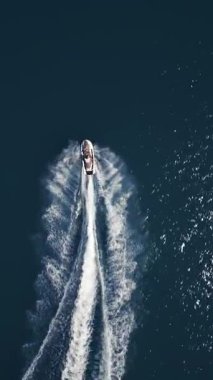 Koyu mavi suda hızla ilerleyen bir jet ski 'nin havadan görünüşü, dinamik beyaz bir iz bırakıyor. Yukarıdan insansız hava aracı tarafından ele geçirildi. Denizde hareketlilik, güç ve yaz eğlencesi sergileniyor..