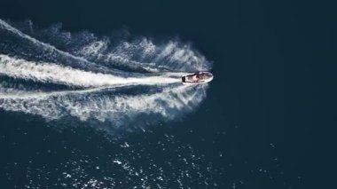 Koyu mavi suda hızla ilerleyen bir jet ski 'nin havadan görünüşü, dinamik beyaz bir iz bırakıyor. Yukarıdan insansız hava aracı tarafından ele geçirildi. Denizde hareketlilik, güç ve yaz eğlencesi sergileniyor..