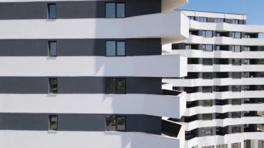 İnsansız hava aracı, beyaz ve koyu gri aksanlı, geometrik balkon ve geniş pencereli modern bir konut binasının ön cephesinde uçuyor..