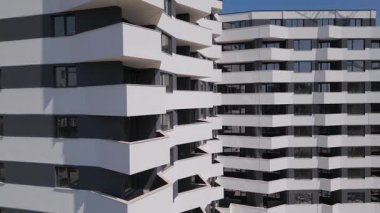 İnsansız hava aracı, beyaz ve koyu gri aksanlı, geometrik balkon ve geniş pencereli modern bir konut binasının ön cephesinde uçuyor..