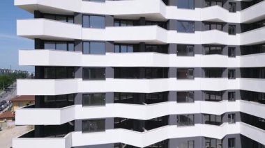 İnsansız hava aracı, beyaz ve koyu gri aksanlı, geometrik balkon ve geniş pencereli modern bir konut binasının ön cephesinde uçuyor..