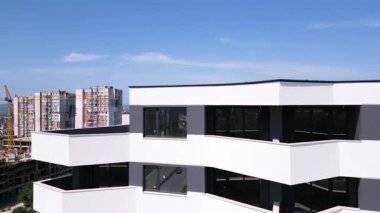İnsansız hava aracı, beyaz ve koyu gri aksanlı, geometrik balkon ve geniş pencereli modern bir konut binasının ön cephesinde uçuyor..