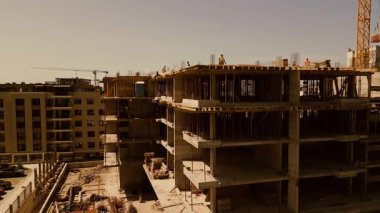 Gün batımında tahta kaldıran vinçli inşaat alanı. İşçiler ve inşaat malzemeleri. Sanayi gelişimi ve ağır ekipman silueti.