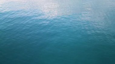 Sakin mavi su yüzeyinde hafif dalgalar ve yumuşak ışık yansımaları. Tasarım, rahatlama veya refah temaları için minimalist doğal arkaplan.