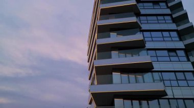Alacakaranlıkta parıldayan LED çizgileri ve cam balkonları olan modern yüksek binalar. Yumuşak pastel bir gökyüzüne karşı zarif şehir mimarisi.