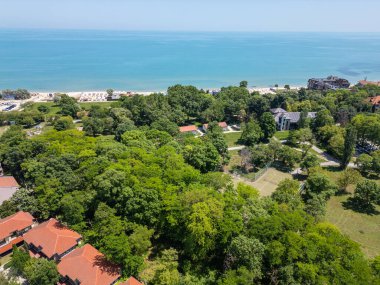 Sahili, tenis kortu ve kırmızı çatısı olan yemyeşil ağaçlarla çevrili deniz manzaralı bir tatil köyü. Deniz kenarındaki açık bir günde huzurlu bir yaz mevsimi..