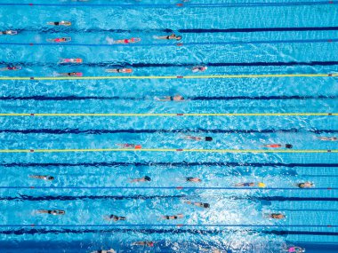 Olimpik boyutta bir havuzda yüzücülerin eğitimini yukarıdan aşağıya gösteren bir görüntü. Hareket halindeki insanlarla dolu bir sürü şerit. Açık mavi suyla aktif yaz sporları ve fitness sahnesi.