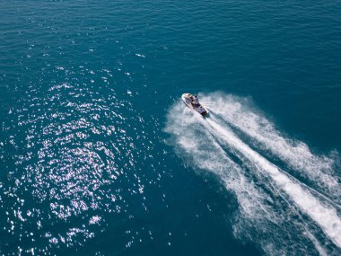 Koyu mavi suda hızla ilerleyen bir jet ski 'nin havadan görünüşü, dinamik beyaz bir iz bırakıyor. Yukarıdan insansız hava aracı tarafından ele geçirildi. Denizde hareketlilik, güç ve yaz eğlencesi sergileniyor..