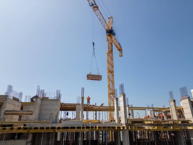 İşçiler ve büyük sarı bir vinç ile kentsel inşaat alanı modern bir şehir mahallesinde yeni bir yerleşim yeri inşa ediyor, arka planda bir şehir manzarası ve tepeleri var..
