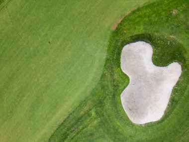 Yeşil çim yolları, kum sığınakları, golf arabaları ve oyuncularla dolu, yemyeşil bitki örtüsü ve turkuaz deniz manzaralı bir sahil golf sahası manzarası..