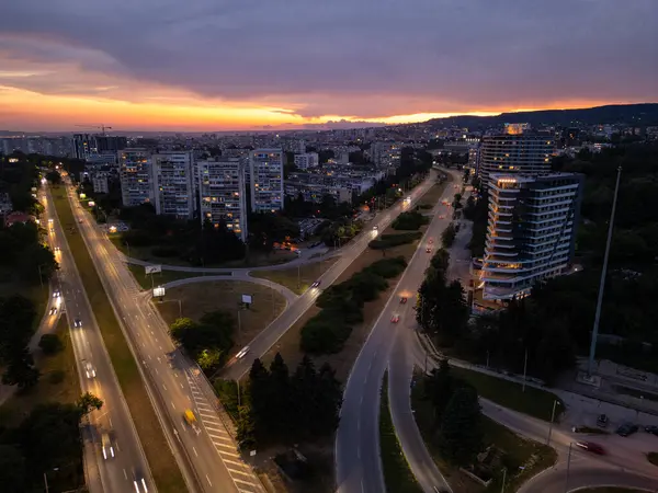 Bulgaristan 'ın Varna kentinde günbatımında havadan panoramik manzara. Karadeniz üzerinde kıyı kenti ışıkları, konut binaları, otoyollar ve dramatik gökyüzü bulunan şehir manzarası.