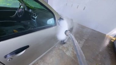 Otomobil yıkamada yüksek basınçlı hortumla araba yıkarken yavaş çekim. Su, araçların yüzeyine köpük yayılırken yan ayna ve kapıya sıçrar..