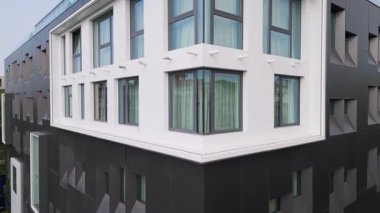 Köşedeki pencereleri ve geometrik cephesi olan modern siyah beyaz bir binanın videosu. Temiz çizgileri ve perdelerle kaplı cam panelleri olan çağdaş şehir mimarisi.