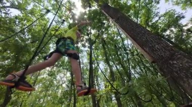 İki çocuk ağaçların arasına halat macerası parkına tırmanıyor, emniyet kemerleri takıyor ve güneşli bir günde heyecan verici bir açık hava aktivitesinin tadını çıkarıyorlar..