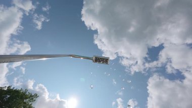 Açık hava duşunun yavaş çekim gücü mavi gökyüzüne ve güneşe su damlacıkları püskürterek parlak bokeh ve yaz atmosferini oluşturur.