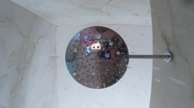 Çağdaş bir tavan yağmurundan akan su seramikli bir banyoda, buzlu camdan gelen güneş ışığı temiz ve taze bir atmosfer yaratıyor..