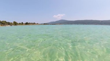 Uzak ormanlık tepeleri ve ufukta bir yatı olan turkuaz deniz suyunun manzarası. Sakin dalgalar ve parlak yaz gökyüzü huzurlu bir tatil ortamı yaratır..